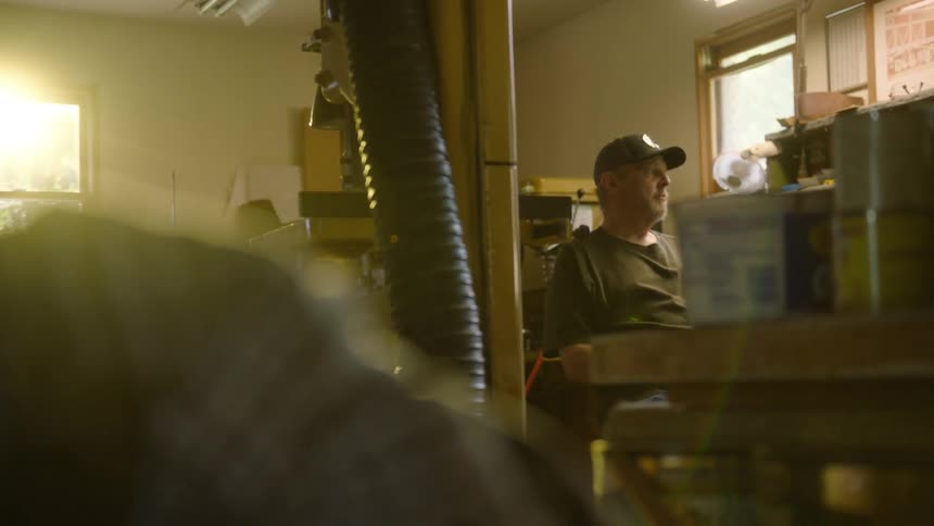 A craftsman sits thoughtfully in his workshop as the warm afternoon sun streams in through the window