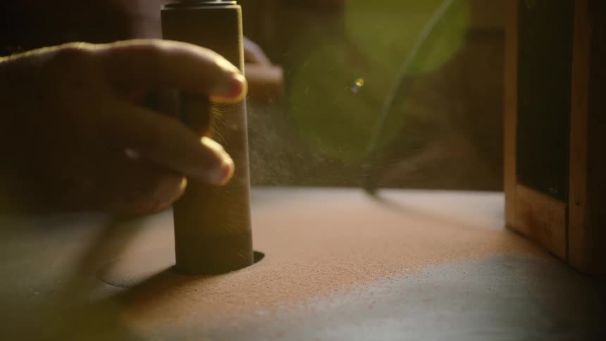 A close-up slow-motion shot shows fine sawdust flying off a piece of wood as it's being shaped on an oscillating spindle sander in a workshop