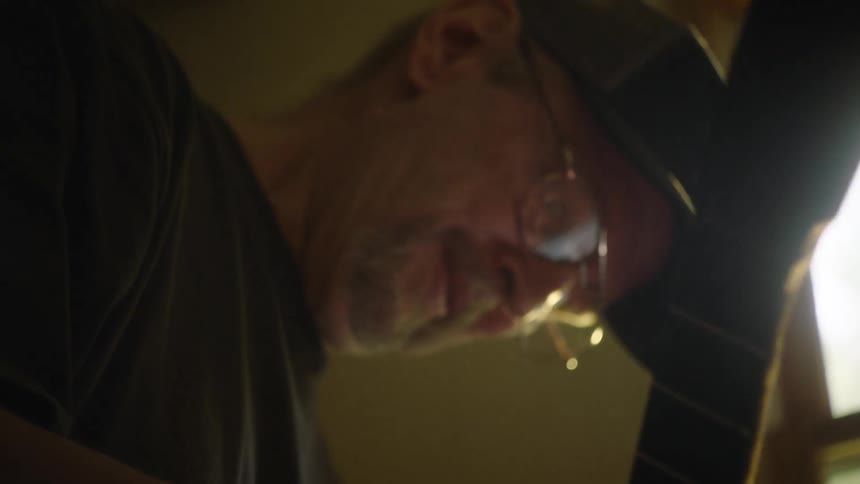 A focused luthier meticulously sands the neck of a guitar, with sawdust dancing in the warm backlight of his workshop