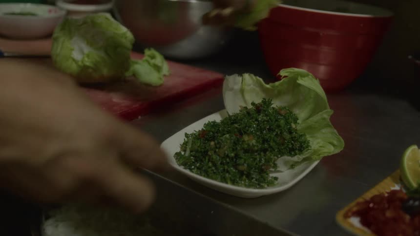 A chef squeezes fresh lime over a tabbouleh salad, garnishing the dish with a lime wedge in a professional kitchen