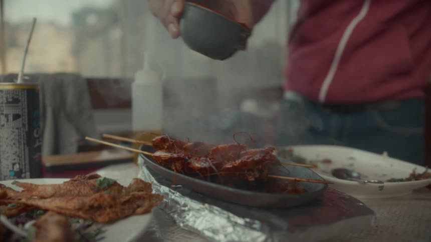 A chef pours a red sauce over sizzling hot grilled shrimp skewers at a restaurant table