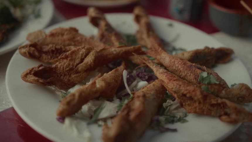 A freshly served plate of golden brown fried fish garnished with herbs on a restaurant table