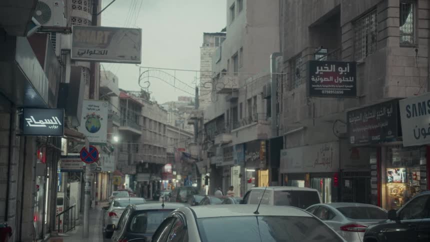 A bustling street in Amman, Jordan is filled with cars and shops on a cloudy day