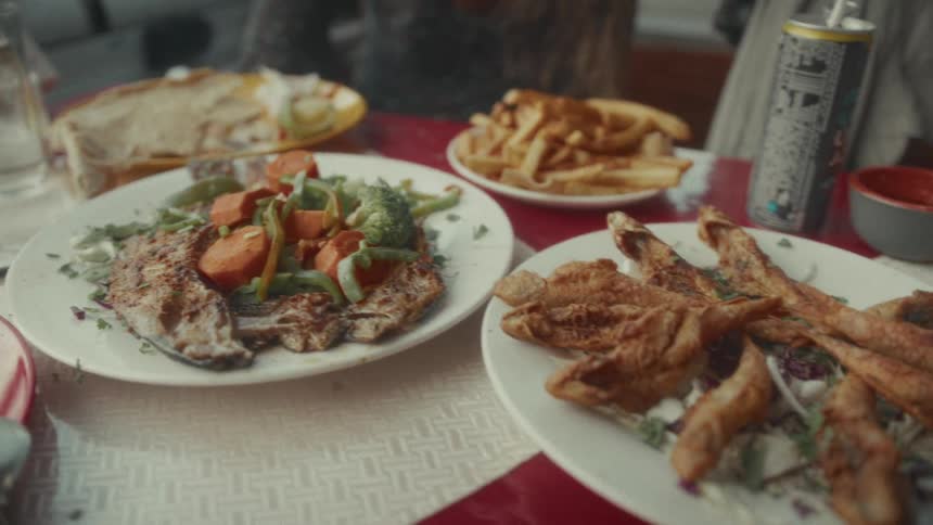 A close-up slow-motion pan across a table laden with fresh seafood dishes, including grilled fish, fried fish, and french fries at a restaurant