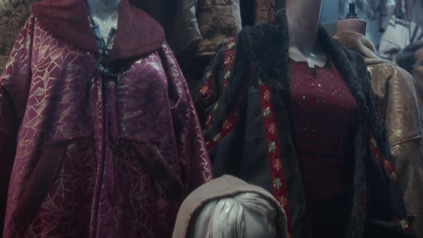 Worn mannequins displaying traditional embroidered coats and jackets in a dimly lit market stall