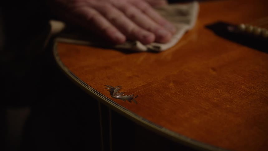 A craftsman gently polishes the wooden body of an acoustic guitar with a soft cloth in slow motion
