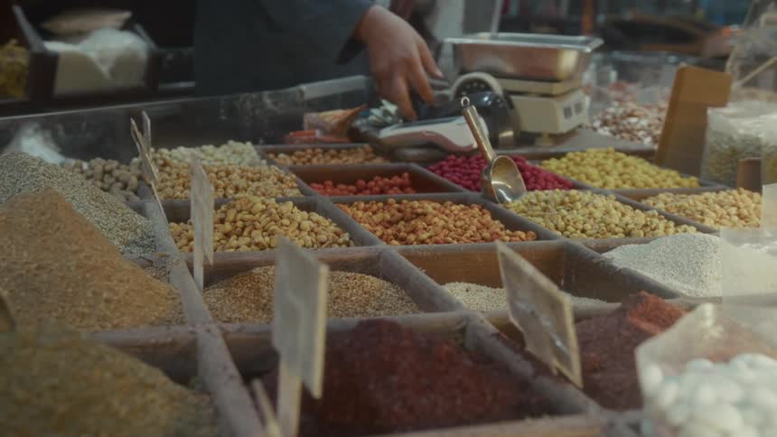 Vibrant display of various nuts, grains, and spices at a bustling market stall while a vendor weighs goods