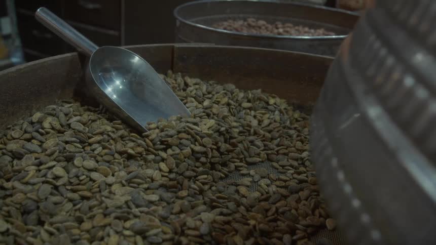 A static close-up shot of a rustic wooden barrel filled with raw nuts or seeds with a metal scoop at an indoor market
