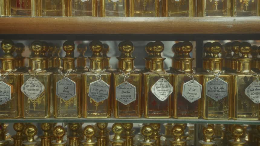 A close-up of ornate golden perfume bottles with Arabic labels displayed on glass shelves in a traditional market shop