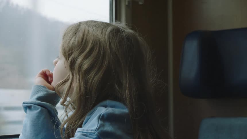 Close-up of a contemplative little girl watching the scenery pass by from a train window