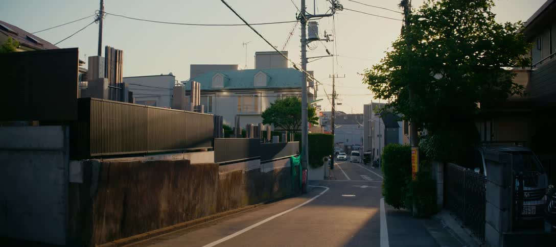 A photographer sets up a tripod to capture the sunset on a quiet residential street in Japan