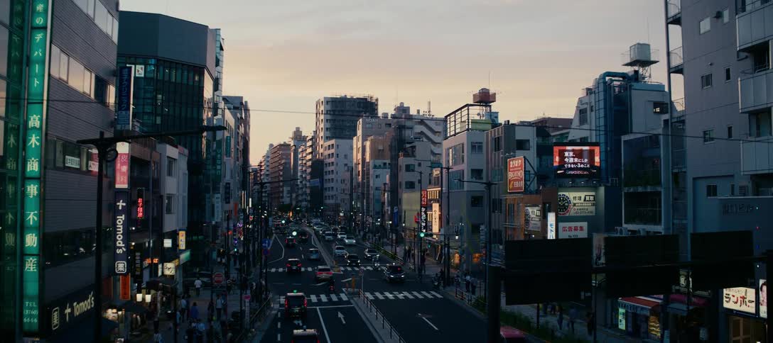 An elevated view shows a bustling city street in Tokyo, Japan with traffic and pedestrians moving below at dusk