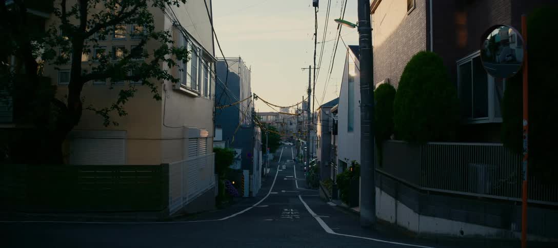 A car drives through a quiet, narrow residential street in a Japanese city at sunset