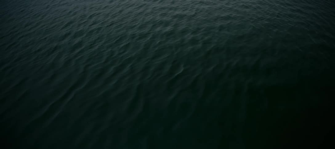 A mesmerizing view from above of dark, calm water with gentle, hypnotic ripples