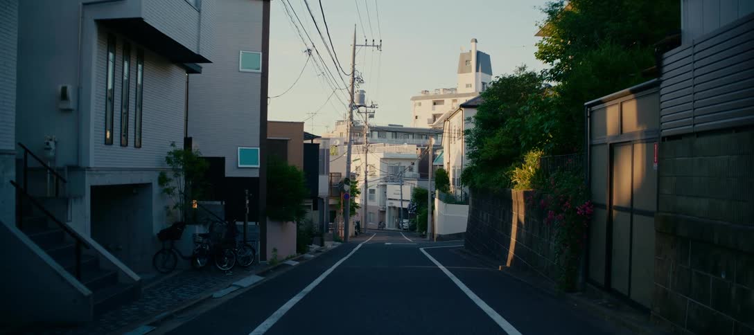 A tranquil view of an empty, sloping residential street in a Japanese city at dawn