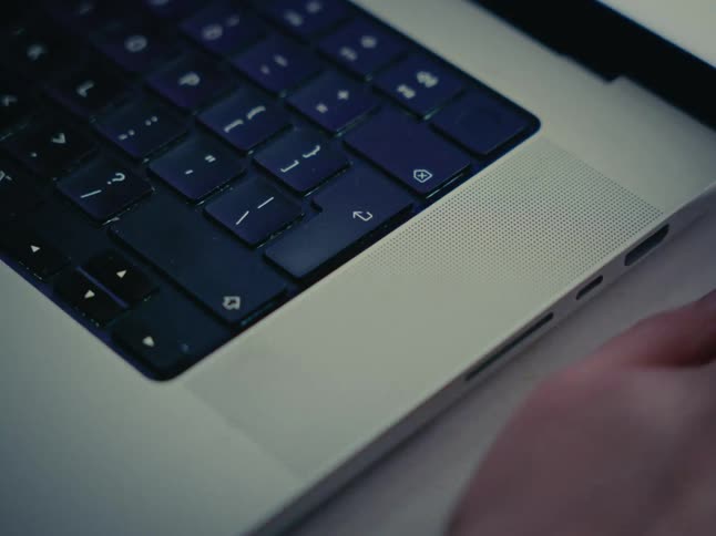 A person's fingers rapidly type on a laptop keyboard in a close-up, out-of-focus shot