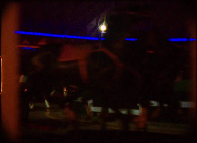 Blurry, dreamlike vintage footage captures a carousel spinning under bright blue lights at an amusement park at night