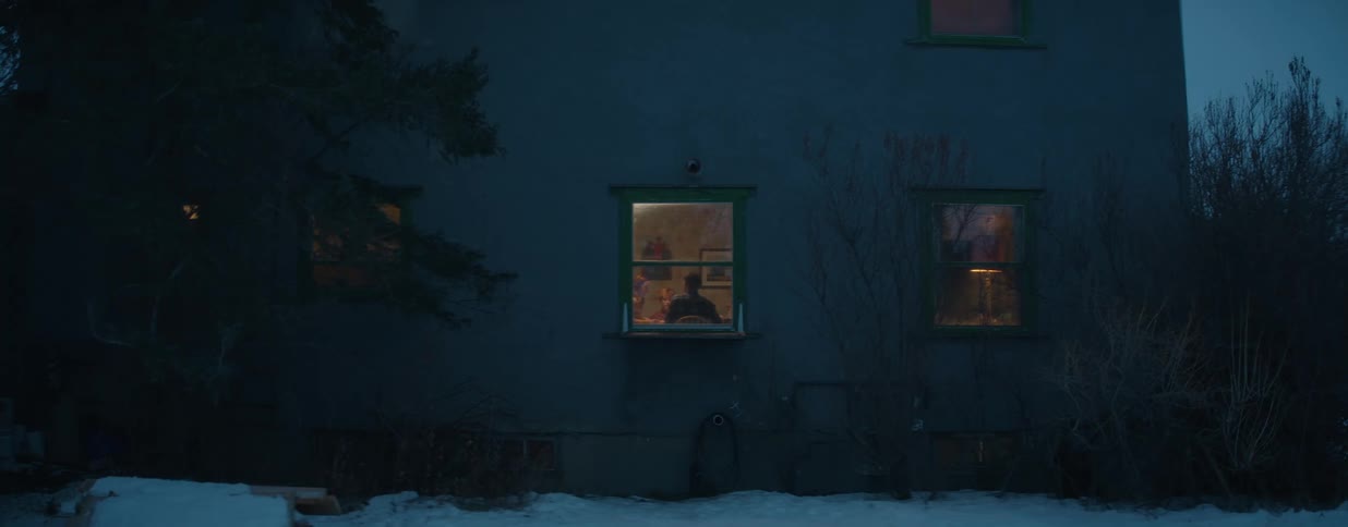 A view from the outside of a family gathered inside their warm, lit home on a cold and snowy winter night