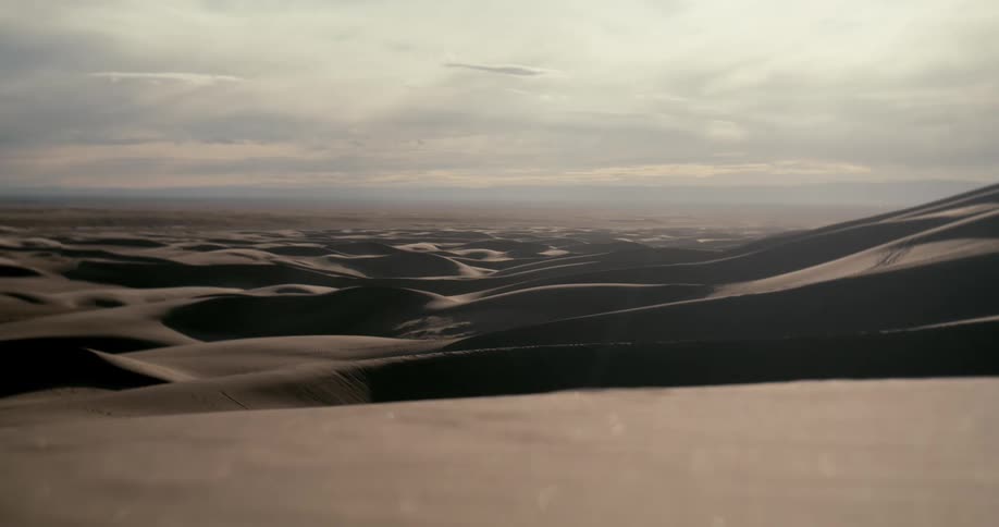 A vast and scenic view of rolling sand dunes under a soft, overcast sky at dusk
