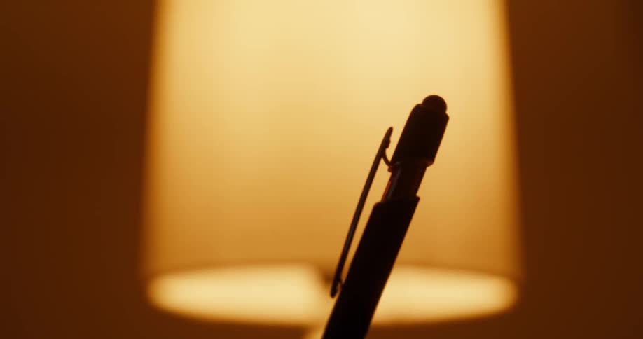 Abstract silhouette of a pen swaying in the warm glow of an out-of-focus lamp