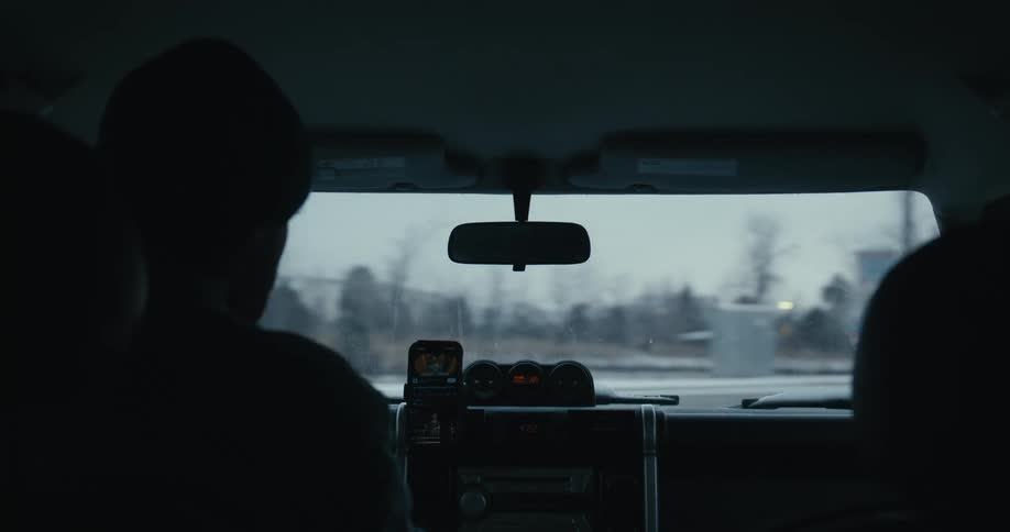 Over-the-shoulder view from inside a car driving through a gloomy, snowy town on a winter day