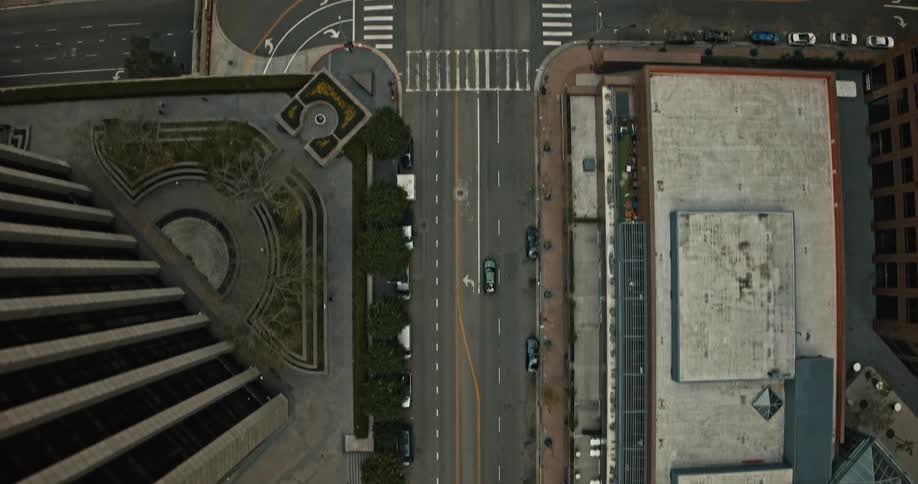 A slow-moving, top-down aerial view of a nearly empty street in a modern city, tracking a single car as it drives along