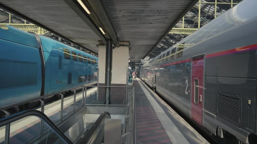 A high-speed train departs from the platform at a bustling European railway station, with passengers waiting to board another train