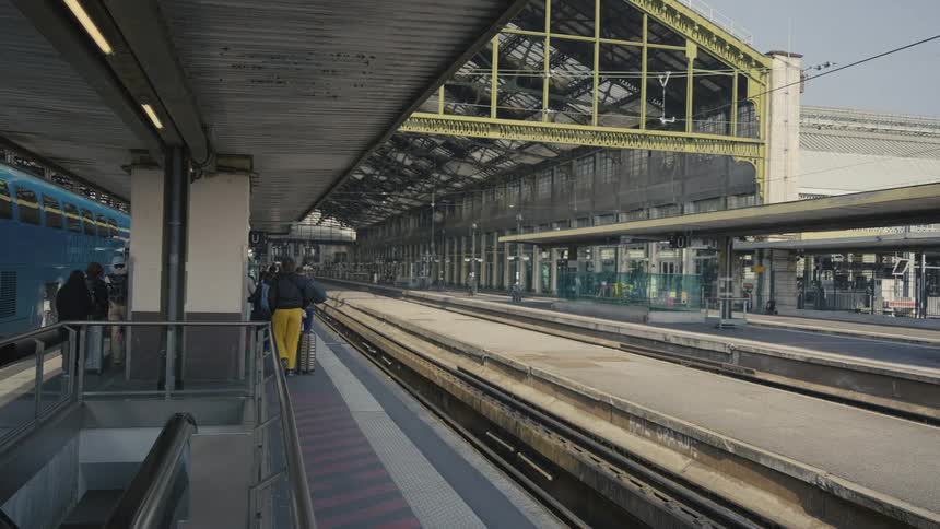 Travelers with their luggage walk in slow motion along the platform at a large train station