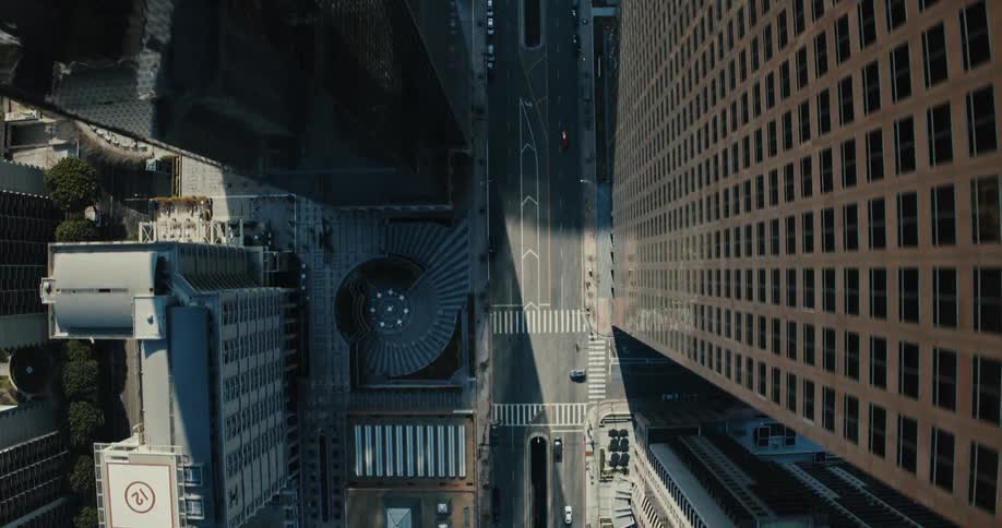 A dramatic top-down aerial shot rises up from a city street canyon nestled between two massive skyscrapers in downtown Los Angeles