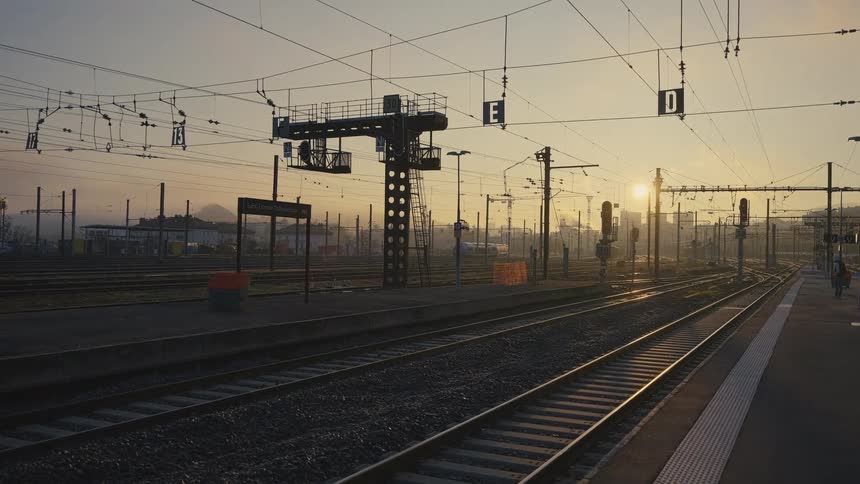 A quiet train station with empty tracks glows in the warm light of sunrise