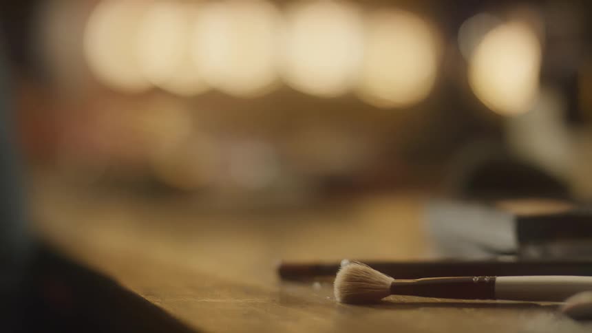 A close-up shot of various artist paintbrushes resting on a wooden table in a warmly lit studio