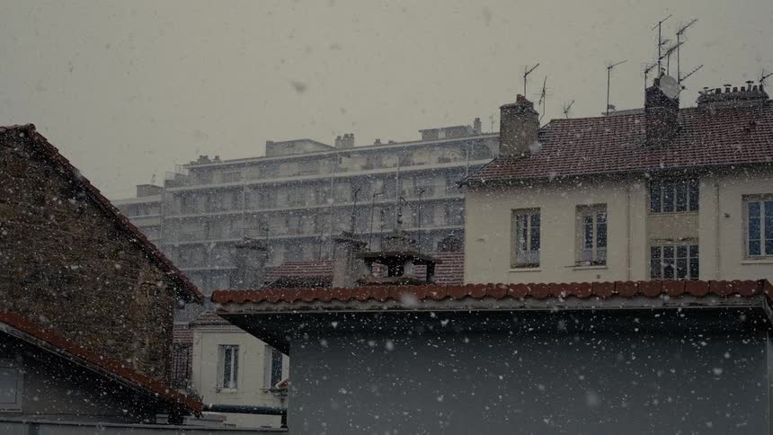 Heavy snow falls over the rooftops of a European city on a quiet winter day