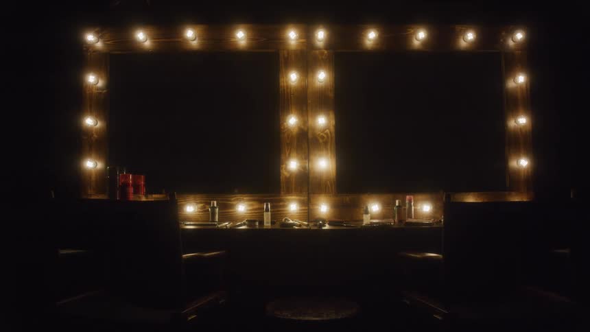 A slow dolly-out reveals a classic wooden makeup mirror with warm incandescent bulbs illuminating an empty dressing room