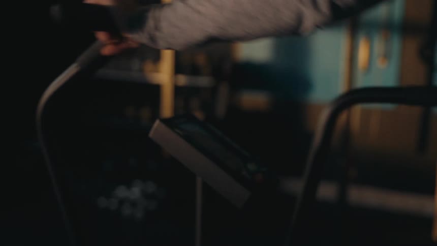 A person wipes down the handles of a piece of workout equipment with a towel in a dark gym