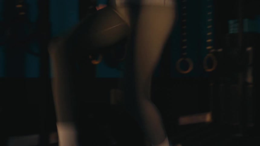 A woman wearing leggings and sneakers performs high knees during a cardio workout in a dark gym