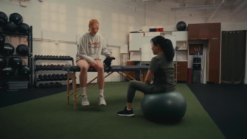 A physical therapist guides her patient through knee rehabilitation exercises in a modern gym setting