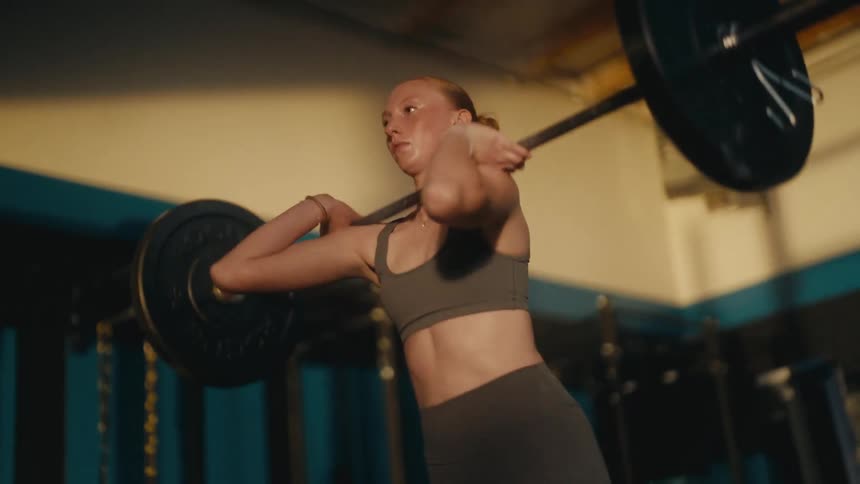 Slow motion shot of a determined woman completing an intense weightlifting repetition with a barbell at the gym