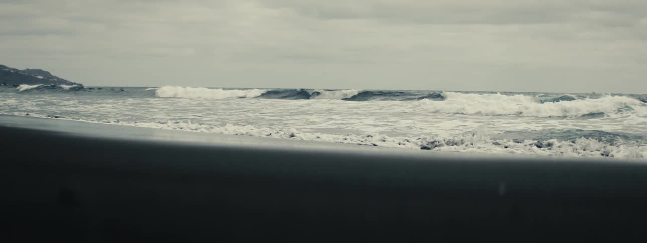 Dramatic slow-motion view of powerful ocean waves crashing onto a dark shoreline under a cloudy sky