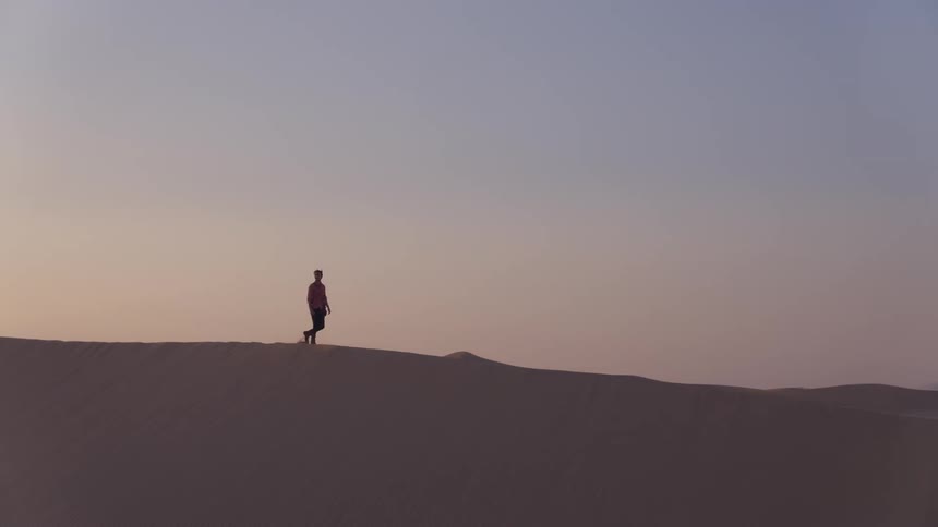 A man walks on a sand dune in a desert
