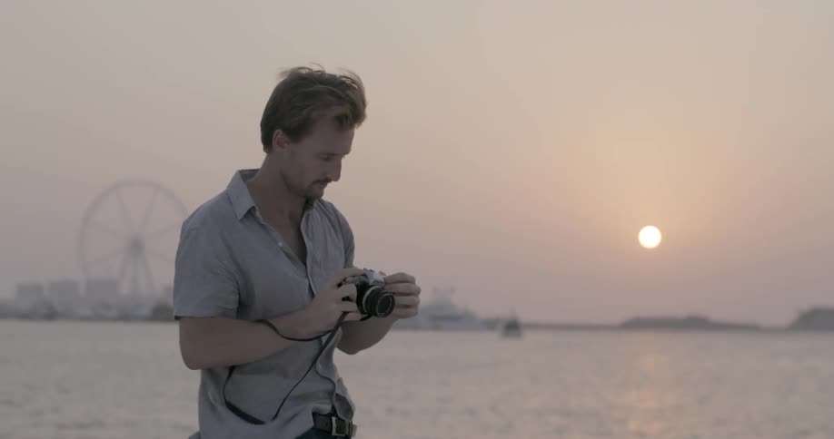 A man stands on the deck of a boat taking photos at dusk