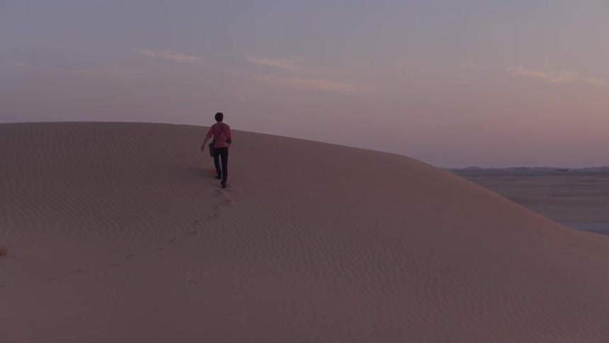 Man walking up hill in sand dunes at dusk