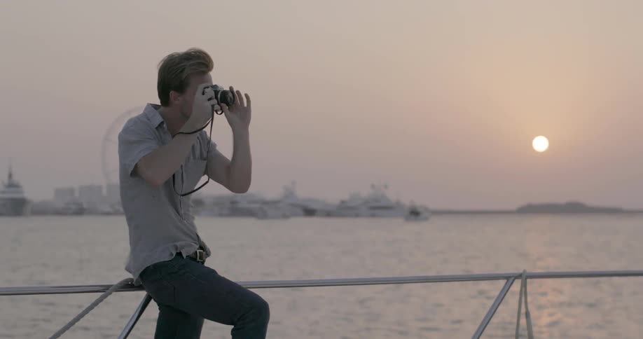 A man sits on a railing taking photographs