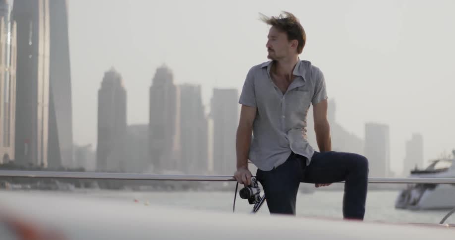 A man is sitting on the railing of a moving boat