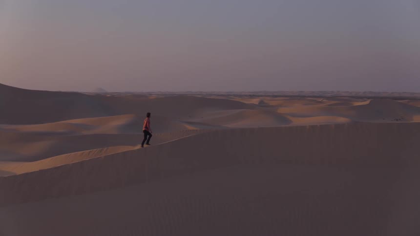 A man is hiking up a sand dune