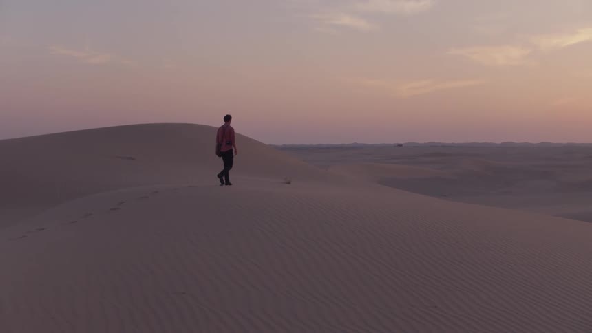 Man walks through the desert at sunset
