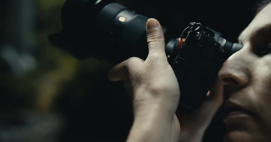Close up of a focused photographer adjusting the lens while looking through the viewfinder in a moody setting