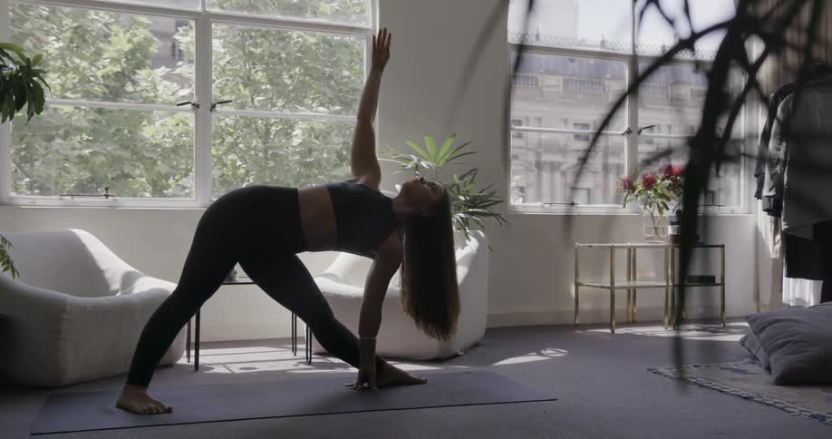 Woman doing yoga pose on mat in living room on sunny day