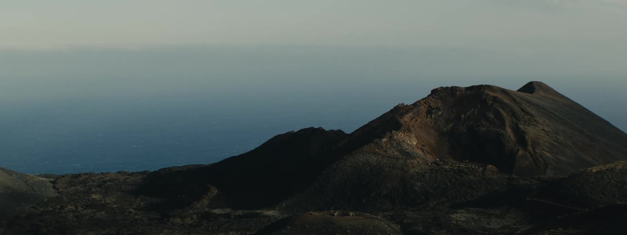 Steam rises from a fumarole on a desolate volcanic mountain overlooking the vast ocean