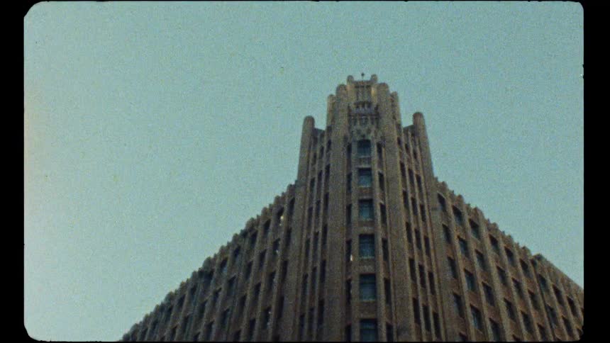 A low-angle shot of an imposing Art Deco building against a clear sky, captured on vintage film