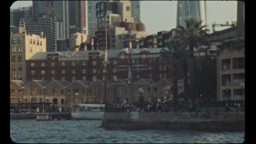 A vintage Super 8 film captures the bustling Sydney harbor waterfront with its historic buildings and modern skyline